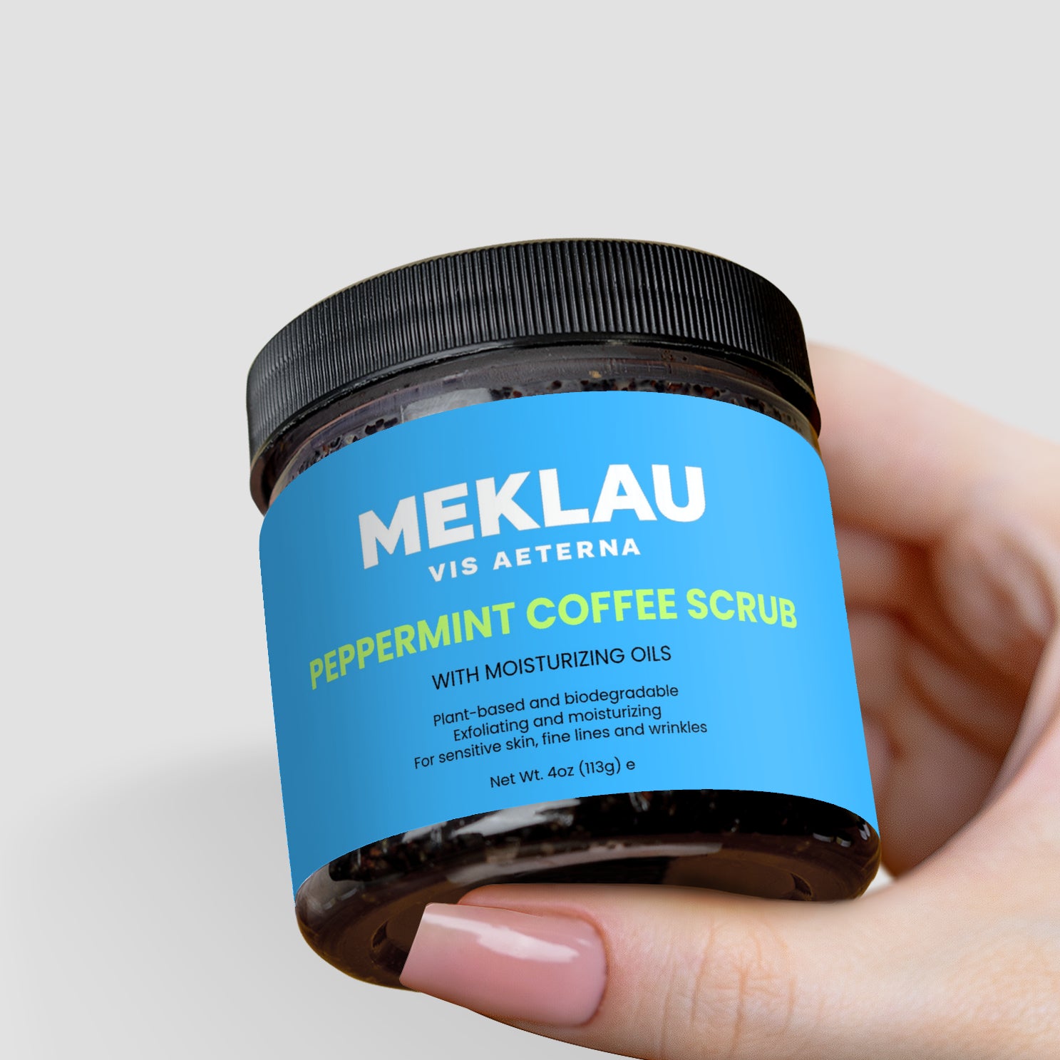 A hand holding a jar of Meklau Vis Aeterna Peppermint Coffee Scrub against a light gray background.